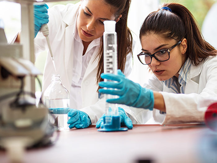 zwei Laborantinnen aus der Pharmaindustrie arbeiten mit Pipette und Glaskolben