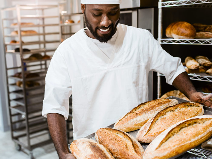 Bäcker aus der Lebensmittelindustrie holt Brote aus dem Ofen